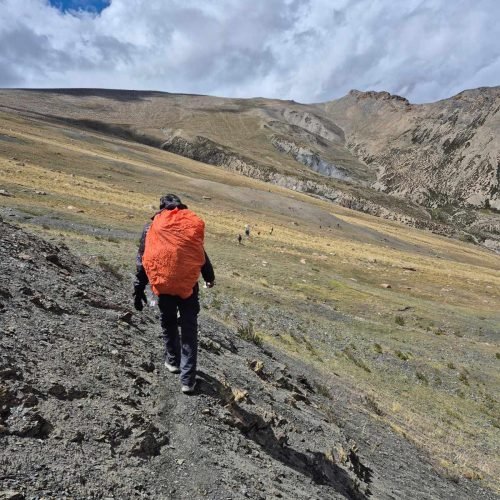 Trekker carrying a red pack cover across a broad alpine valley