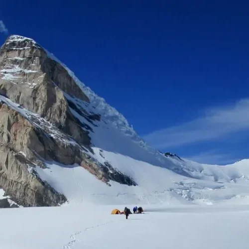 Small expedition camp on a glacier beneath a steep mountain face